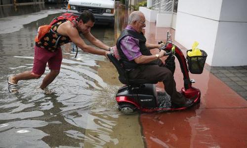 One man pushes another in a wheelchair through Miami floodwaters